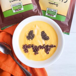 A healthy Halloween smoothie bowl with a jack-o-lantern face made out of chia seeds and cacao nibs.