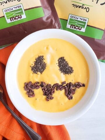 A healthy Halloween smoothie bowl with a jack-o-lantern face made out of chia seeds and cacao nibs.