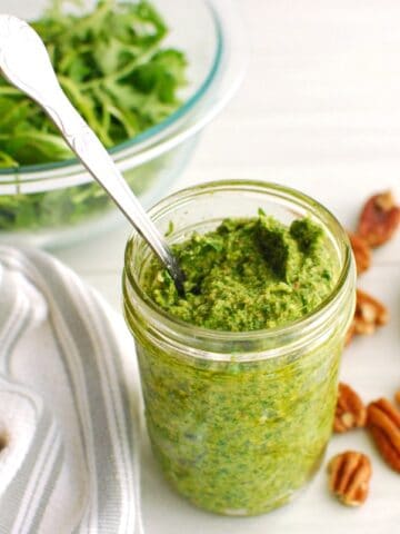 A jar of arugula pesto with a spoon sticking out of the jar, next to a napkin.