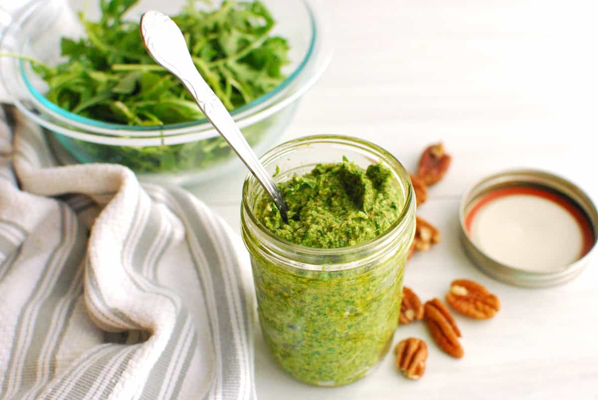A jar of arugula pesto with a spoon sticking out of the jar, next to a napkin.