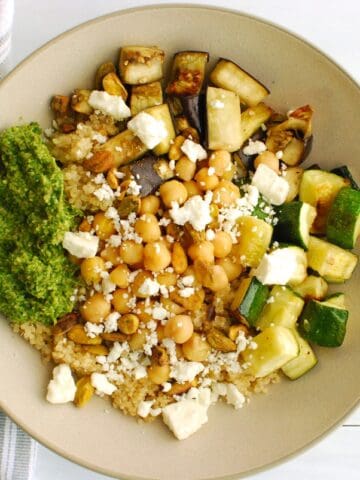 A roasted vegetable and quinoa bowl topped with arugula pesto, feta, and pistachios.