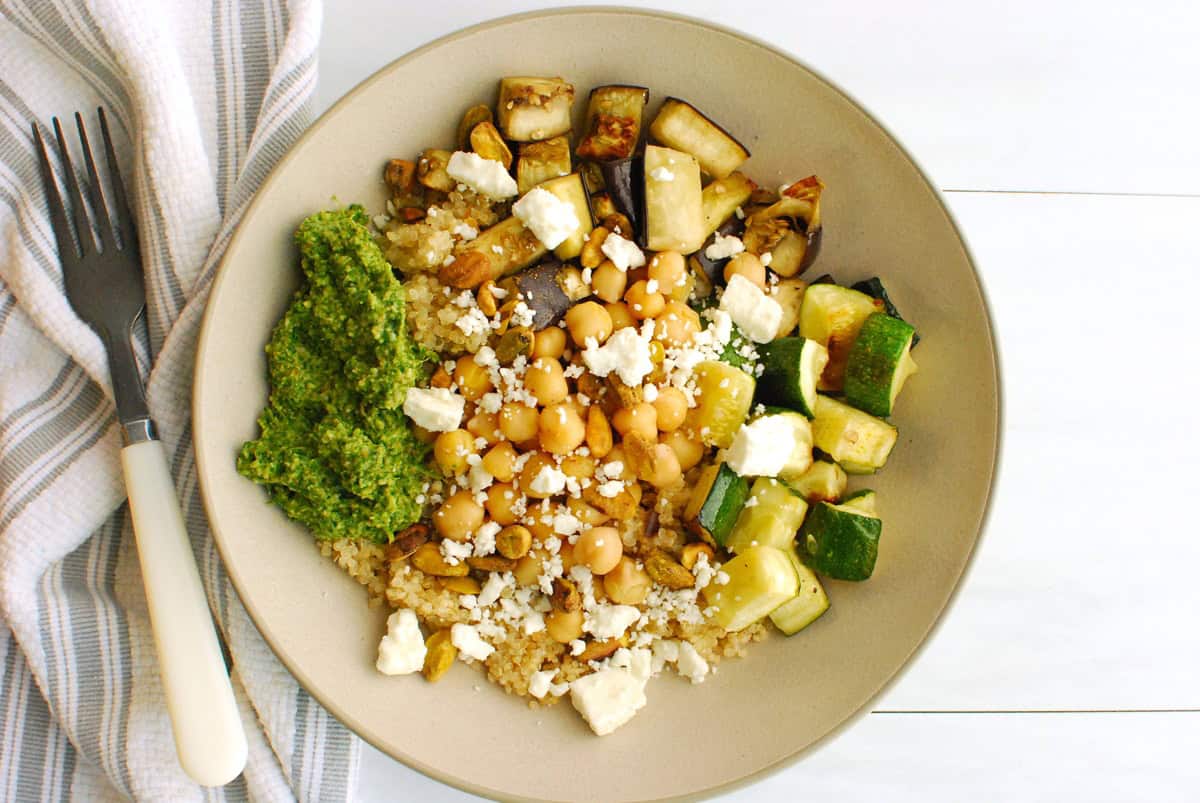 A roasted vegetable and quinoa bowl topped with arugula pesto, feta, and pistachios.